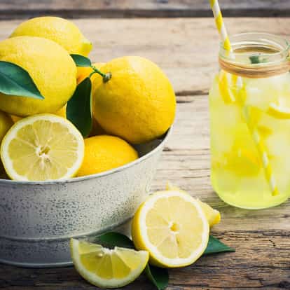 Bitter Lemon in a glass jar with ice and lemon slices beside a metal bowl of whole lemons on a wooden table