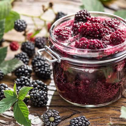 Blackberry puree in a hinged glass jar with whole blackberries and leaves on a wooden board