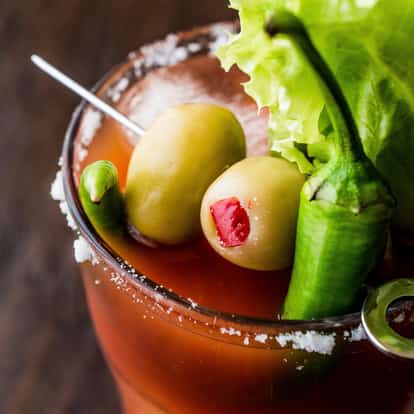 Bloody Mary Mix in a salt-rimmed glass with two skewered olives, a chili pepper and a lettuce leaf