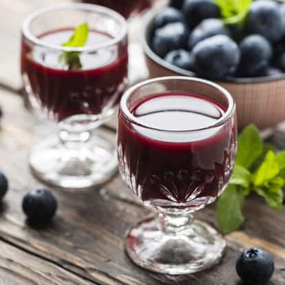 Blueberry Liqueur in two cut-glass cordial glasses on a wooden table with blueberries and mint