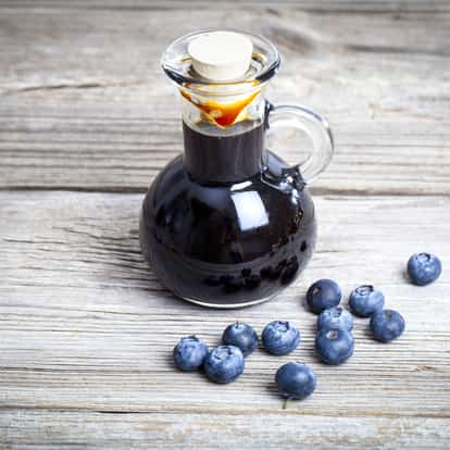 Blueberry Syrup in a glass cruet with scattered blueberries on a wooden surface