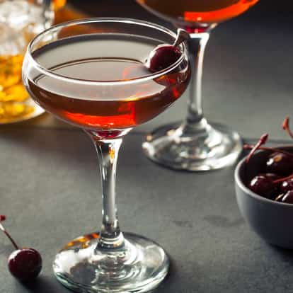 Byrrh in a coupe glass with a maraschino cherry on a dark surface