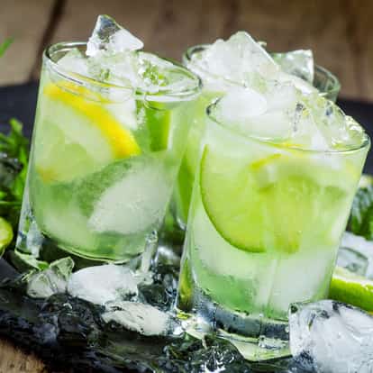 Cachaca in three rocks glasses with crushed ice and lime wedges on dark slate