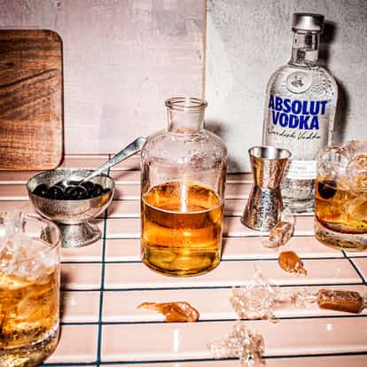 Caramel Syrup in a small glass bottle with an Absolut Vodka bottle and two iced rocks glasses