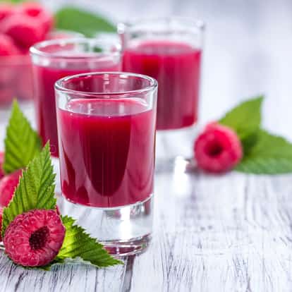 Raspberry liqueur in three shot glasses with raspberries and leaves on white background