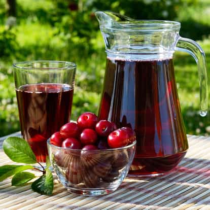 Cherry Juice in a pitcher and a glass with a bowl of cherries on a bamboo mat