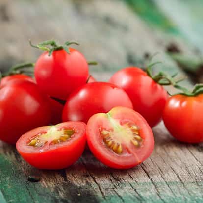 Cherry tomato halved among whole cherry tomatoes on a wooden surface