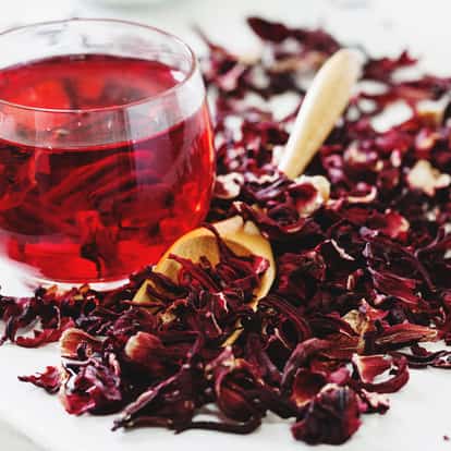 Chilled Hibiscus Tea served in a stemless glass with dried hibiscus petals and a wooden spoon on white background