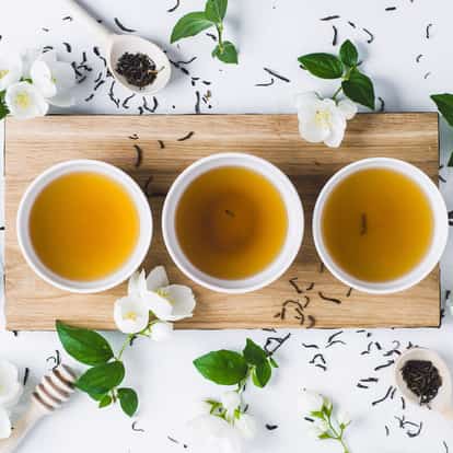 Chilled Jasmine Tea in three bowls on a wooden board with jasmine flowers and loose tea leaves