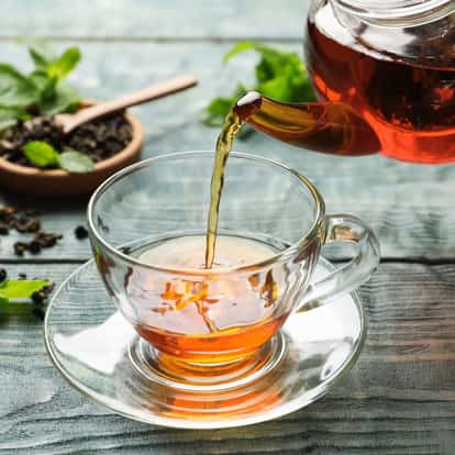 Chilled Lapsang Souchong Tea poured from a glass teapot into a clear glass teacup on a saucer.