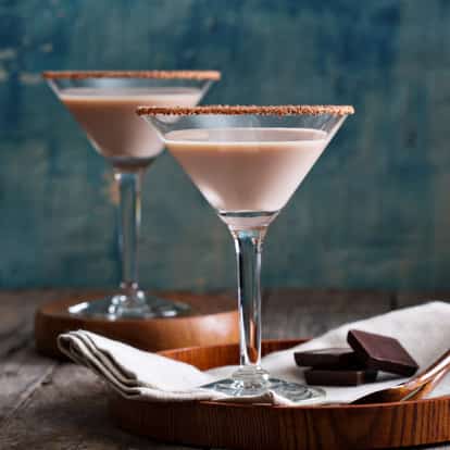 Chocolate Bitters two martini glasses rimmed with grated chocolate on a wooden tray with chocolate squares
