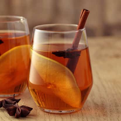 Cinnamon Schnapps Liqueur in a rocks glass with pear slice, cinnamon stick and star anise on a wooden surface