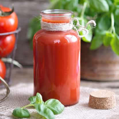 Clamato in a glass jar with twine at the neck, cork stopper beside jar and basil sprig on burlap background