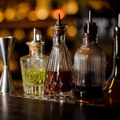Clove Bitters glass bottles with metal pourers and a metal jigger on a bar counter