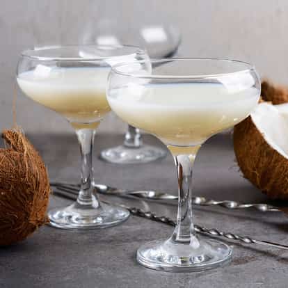 Coconut Liqueur in three coupe glasses with halved coconuts on a table