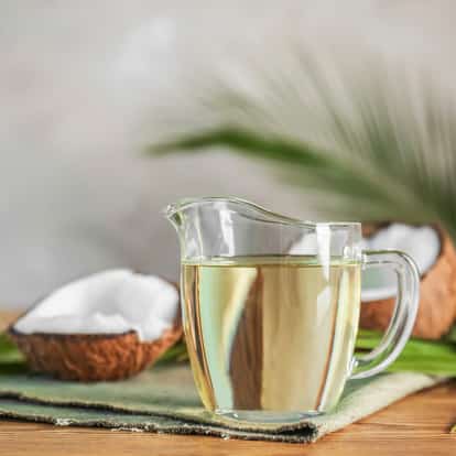 Coconut Syrup in a glass pitcher with halved coconut shells on a linen cloth on a wooden surface