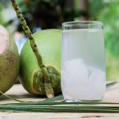 Coconut water in a clear glass with whole coconuts on a wooden surface
