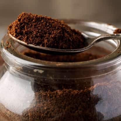 Coffee Ground on a metal spoon above an open glass jar