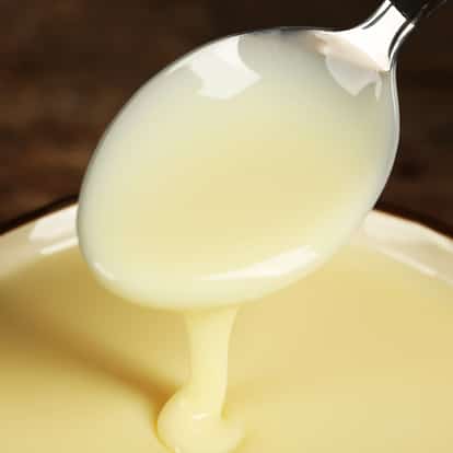 Condensed milk on a spoon dripping into a bowl