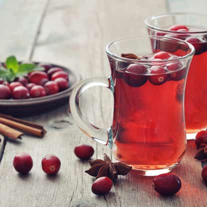 Cranberry Juice (hot) in two clear handled mugs with floating cranberries and star anise on wooden table