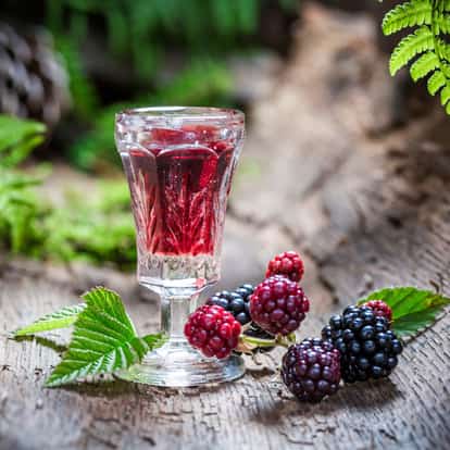 Créme de Mure in a cut cordial glass with blackberries and leaves on a wooden surface