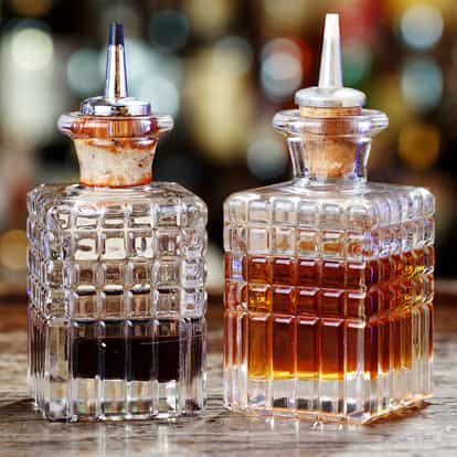 Cucumber Bitters in two square glass bottles with pourers on a wooden surface