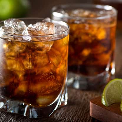 Dark Rum (aged) in a rocks glass with ice and a lime wedge on a wooden board
