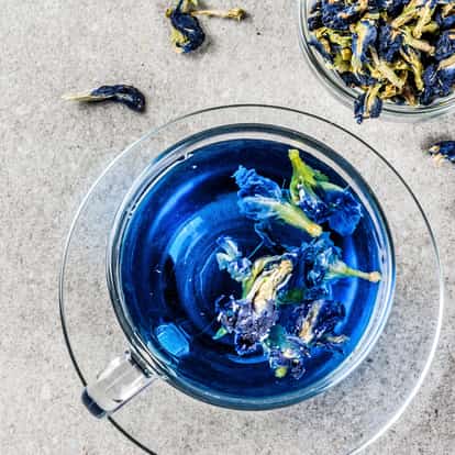 Dried Butterfly Pea Blossom in a glass teacup with loose blossoms and a small glass bowl of dried flowers