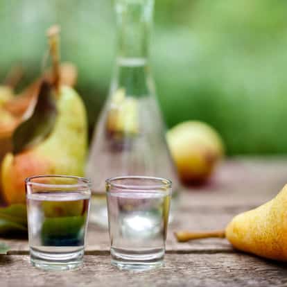 Eau de Vie in two shot glasses on a wooden table with a glass carafe and pears in the background