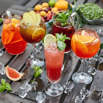 Falernum in assorted glasses on a wooden table with ice cubes and citrus and mint garnishes