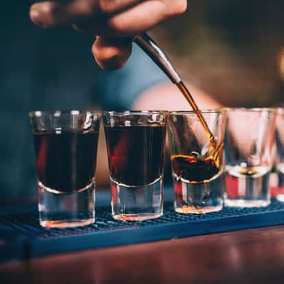 Liqueur shots in a row of four shot glasses with a hand pouring into the third glass