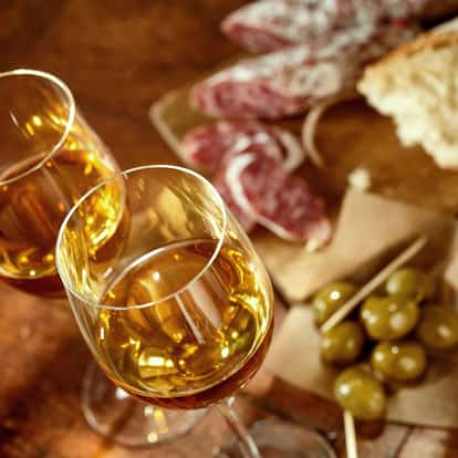Fino Sherry in two wine glasses with olives and sliced salami on a wooden board