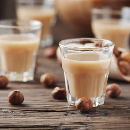 Hazelnut liqueur in a short glass with whole hazelnuts on a wooden surface