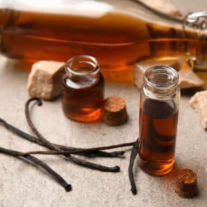 Fresh Homemade Vanilla Cordial in small glass vials with vanilla pods and sugar cubes on a stone surface