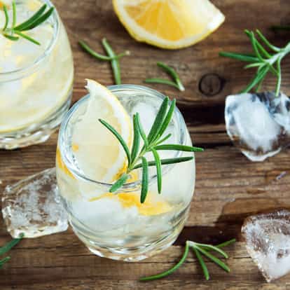 Genever in a rocks glass with ice lemon wedge and rosemary sprig on a wooden surface