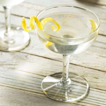 Gin (old Tom) in a coupe glass with a lemon twist on a wooden tabletop