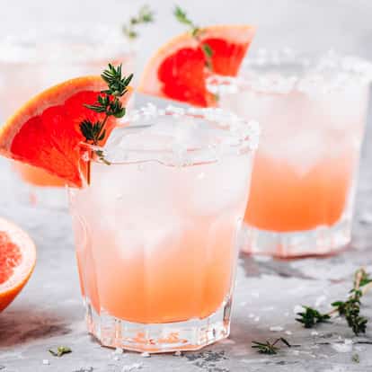 Grapefruit Bitters in a rocks glass with ice and a salted rim with a grapefruit wedge and thyme sprig