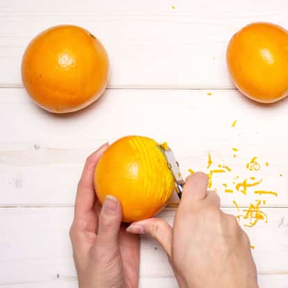 Grapefruit zest peeled from fruit with a zester and hands on a white wooden board