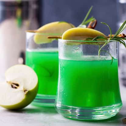 Green Apple Liqueur in two rocks glasses garnished with apple slices and rosemary