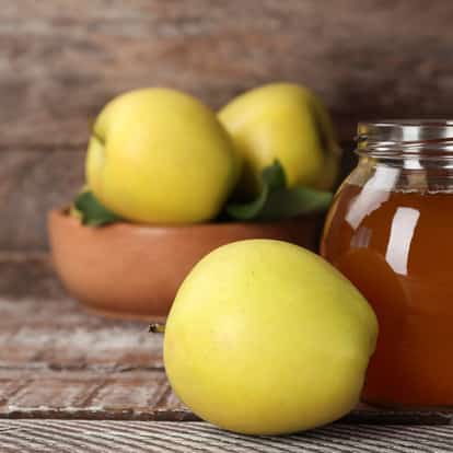 Whole green apples with a jar of amber syrup on a wooden surface.