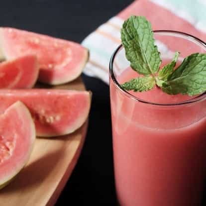 Guava Juice in a tall glass with a mint sprig and sliced guava on a wooden board