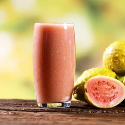 Guava Nectar in a tall glass on a wooden surface with whole and halved guavas beside it
