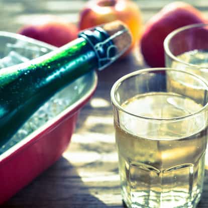 Hard Cider in two tumblers with a bottle on ice and apples in the background