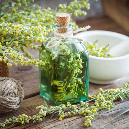 Herbal Liqueur bottle with cork and twine holding sprigs of flowering herbs beside a mortar on a wooden table