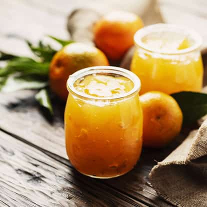 Homemade Marmalade in a small glass jar with a second jar and whole oranges on a wooden surface