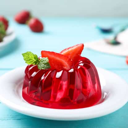 Instant Gelatin molded into a fluted ring on a white plate with sliced strawberry and a mint sprig