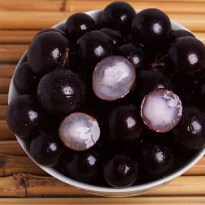 Jabuticaba whole and halved fruits in a ceramic bowl showing pulp on a bamboo mat