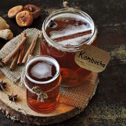Kombucha in a labeled jar and a small glass with a cinnamon stick and dried figs on a wood slice