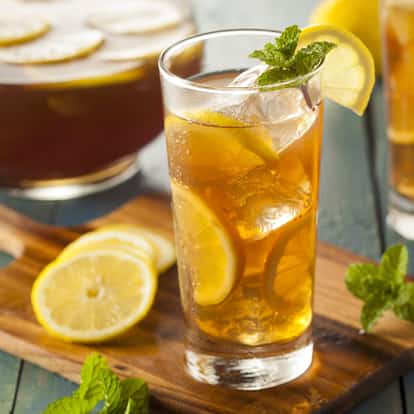 Lemon Iced Tea in a tall glass with ice and lemon slices garnished with mint on a wooden board