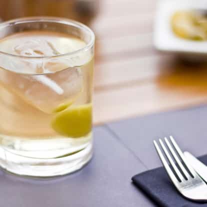 Rose in a rocks glass with ice and an olive on a wooden table